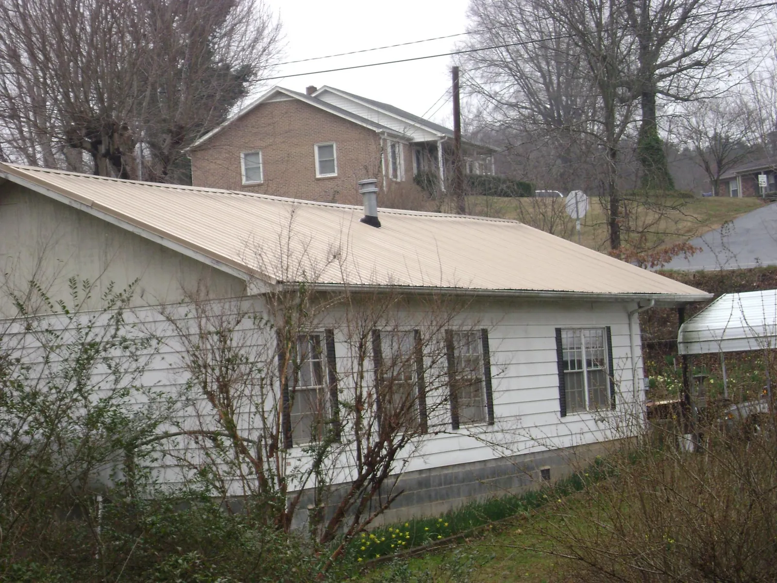 Tan metal roof on a white sided house set into a hillside — Commercial Roofing by Roofing Brothers in Gilbert